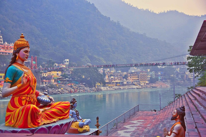 A river with a bridge, a statue of a deity, and a cityscape in the background. 3
