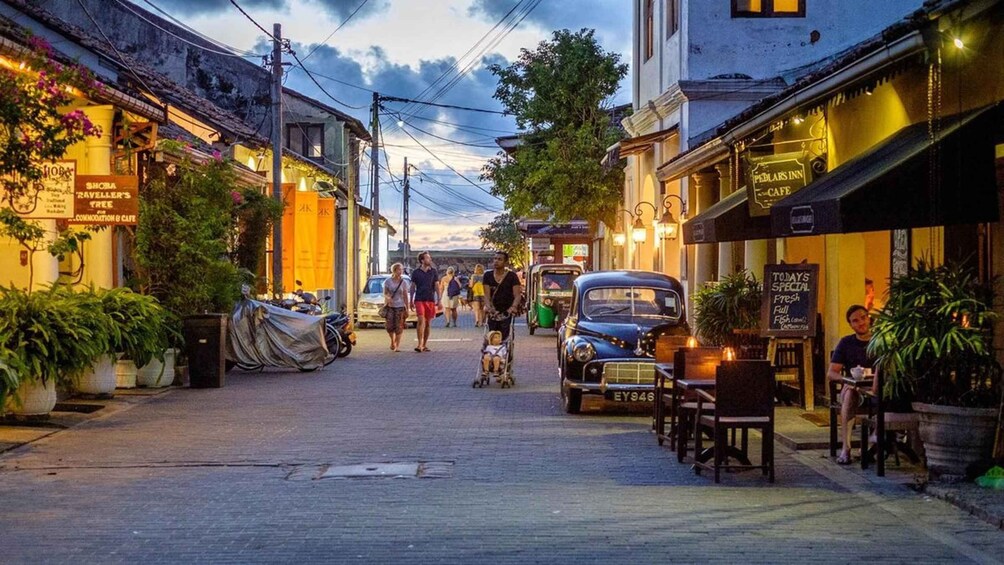A street with shops, a parked car, and people walking. 2