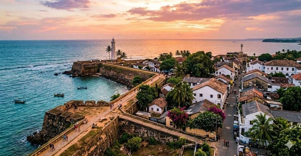 A coastal town with a fort, boats, and a sunset. 1