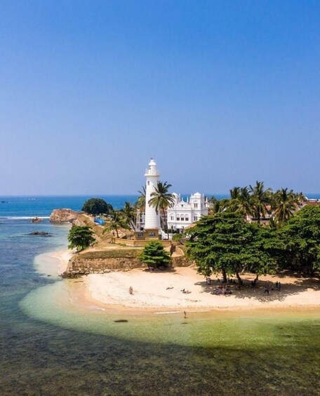 A coastal scene with a white lighthouse, a white building, and palm trees. 3