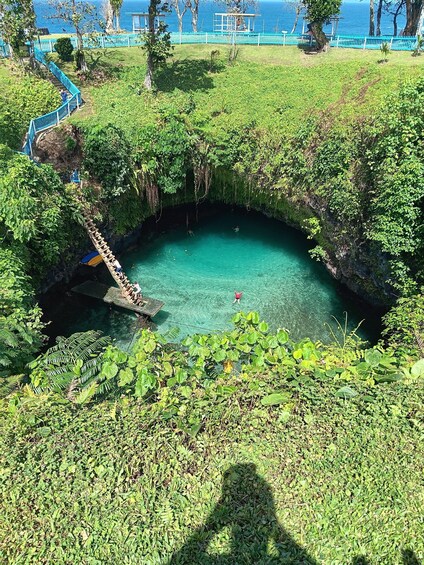 A natural pool surrounded by lush greenery, with a wooden bridge leading into it. 2