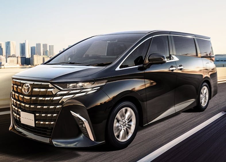 A black Toyota minivan driving on a highway with a city skyline in the background. 4