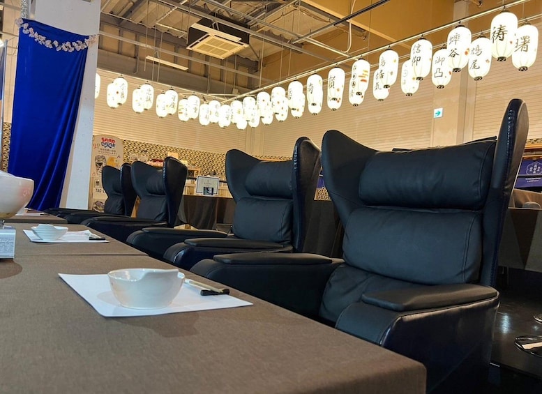 A restaurant interior with black leather chairs, a long table with a white bowl and papers, and traditional Japanese lanterns hanging from the ceiling. 2