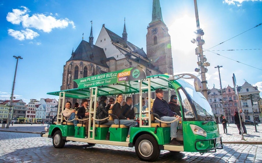 A green tour bus with passengers, parked in front of a historic building with a clock tower. 1