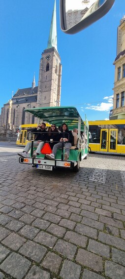 A green and yellow trolley with passengers, a historic building with a clock tower, and cobblestone streets. 3