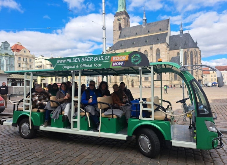 A green tour bus with passengers holding beer mugs, parked in front of a historic building. 5