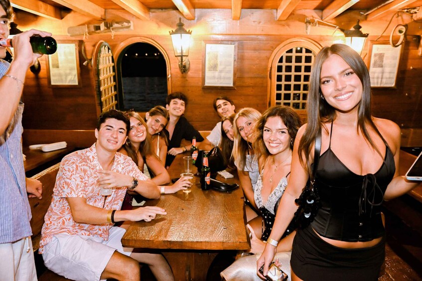 A group of people sitting at a wooden table in a rustic setting with arched windows and wall-mounted lanterns. 1