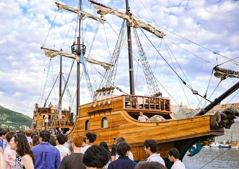 A wooden sailing ship docked at a harbor with a crowd of people around it. 5