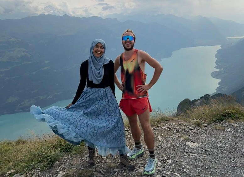 Two people standing on a mountain path with a lake and mountains in the background. 1