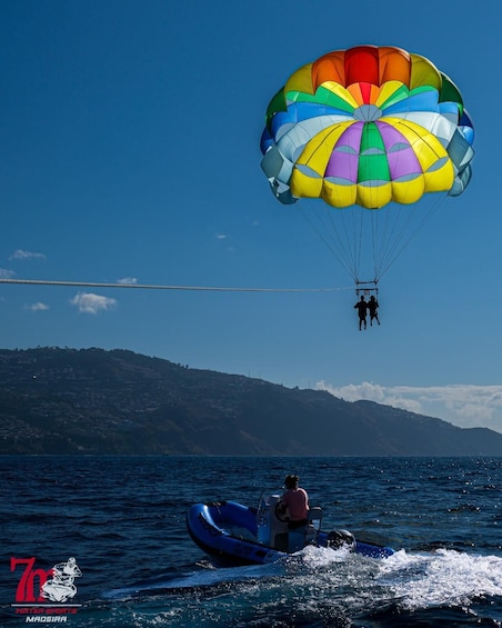 A person parasailing over water with a colorful parachute, a boat, and a hilly landscape in the background. 5