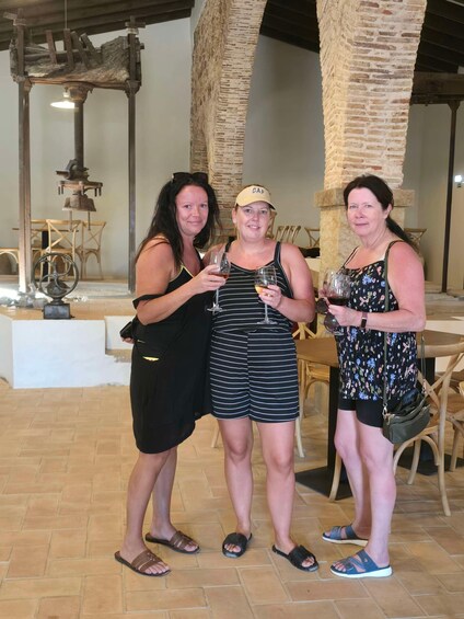 Three people standing indoors, holding wine glasses. 1