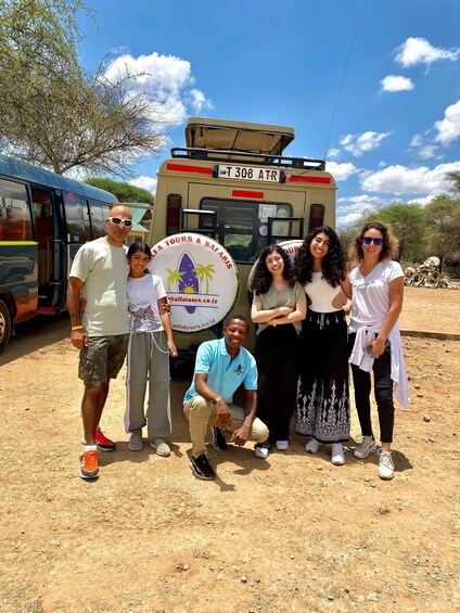Un grupo de personas posando frente a un autobús para safari con un logotipo e información de contacto. 1