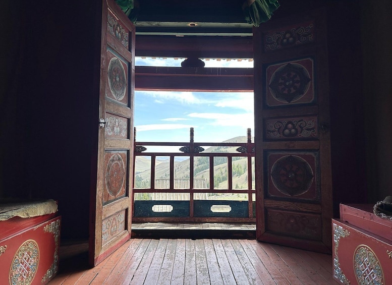 An open wooden door with intricate carvings, leading to a balcony with a view of a mountainous landscape. 2