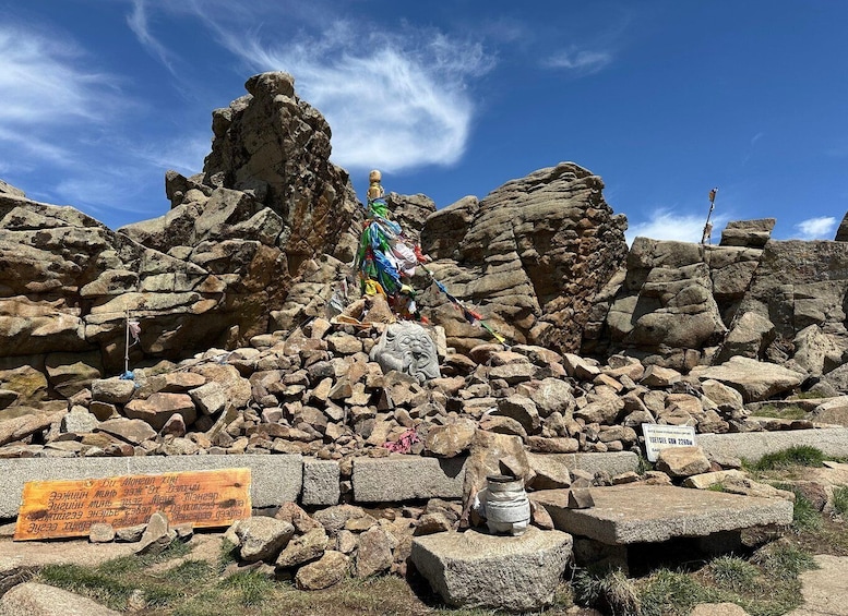 A rocky mountain peak with prayer flags and a sign. 1