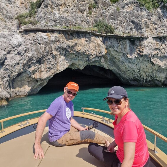 Two people on a boat near a rocky cave entrance with clear water. 5