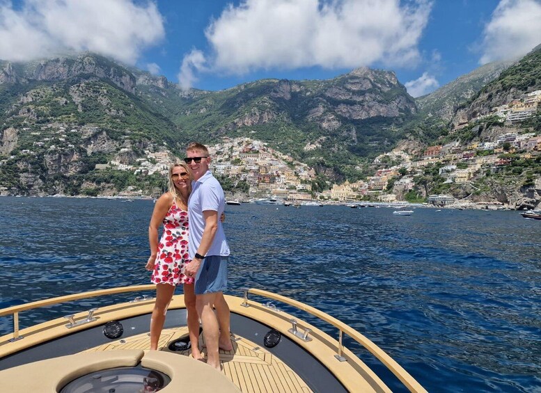 A couple on a boat with a coastal town and mountains in the background. 4