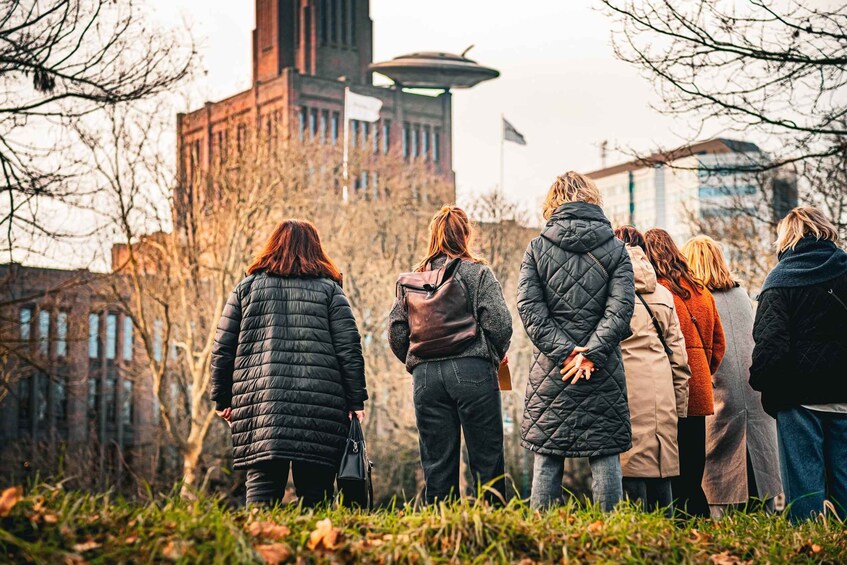 A group of people standing outdoors, facing a building with a large circular structure on top. 3