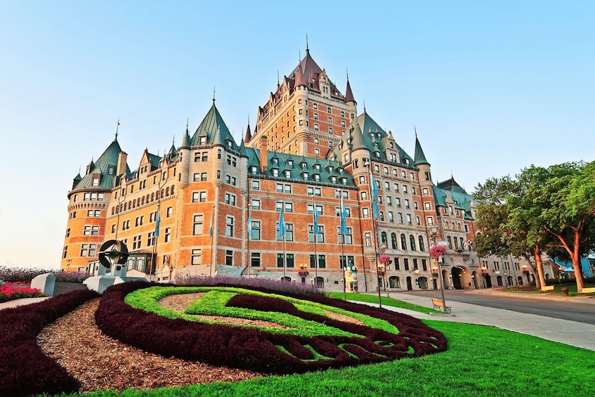 A large, historic building with multiple towers and a landscaped garden. 1