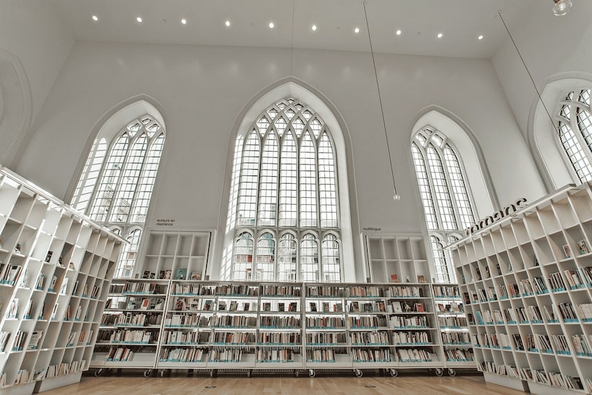A spacious library with high arched windows and white shelving units filled with books. 3