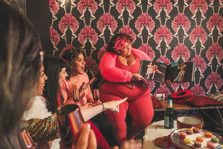 A woman in a red dress holding a framed picture, surrounded by people at a party with drinks and snacks. 4