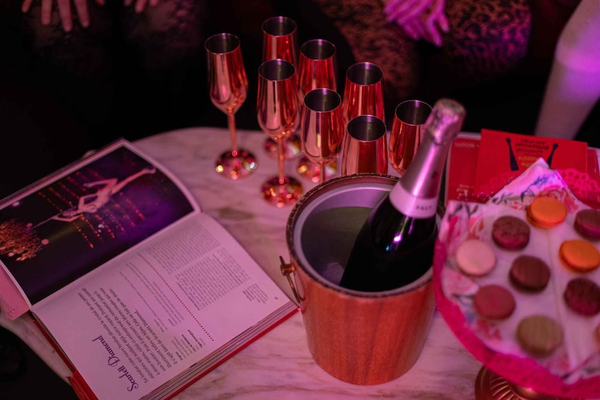 A book, a copper mug with a bottle, glasses, and a plate of macarons on a table. 2
