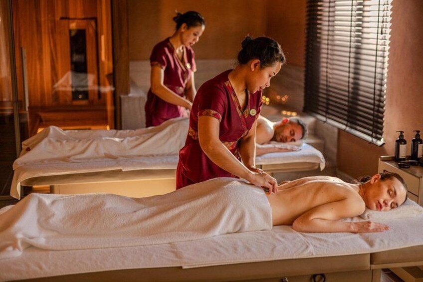Een massageruimte met twee massagetafels, waarvan er een in gebruik is door een gast en de andere door een therapeut. 2