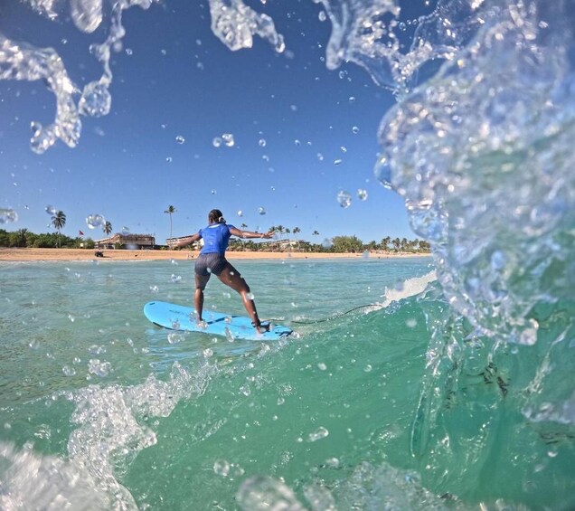 A person surfing on a clear blue water body with a beach and palm trees in the background. 5