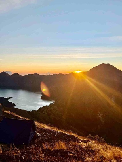 A sunset over a mountainous landscape with a body of water and a tent in the foreground. 1