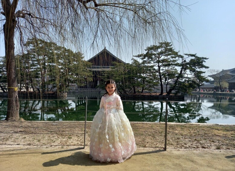 A person in a traditional dress standing in front of a pond with a building in the background. 4