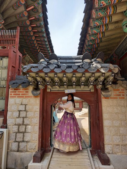 A traditional Korean gate with intricate roof tiles and a person in a purple hanbok entering. 3
