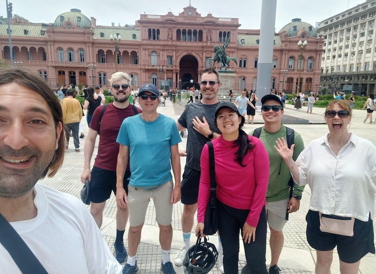 A group of people standing in front of a large pink building with a statue in the center. 5