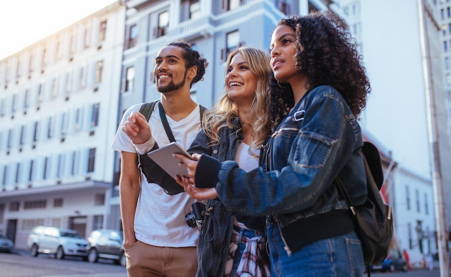 Three people standing on a city street, one holding a tablet. 2