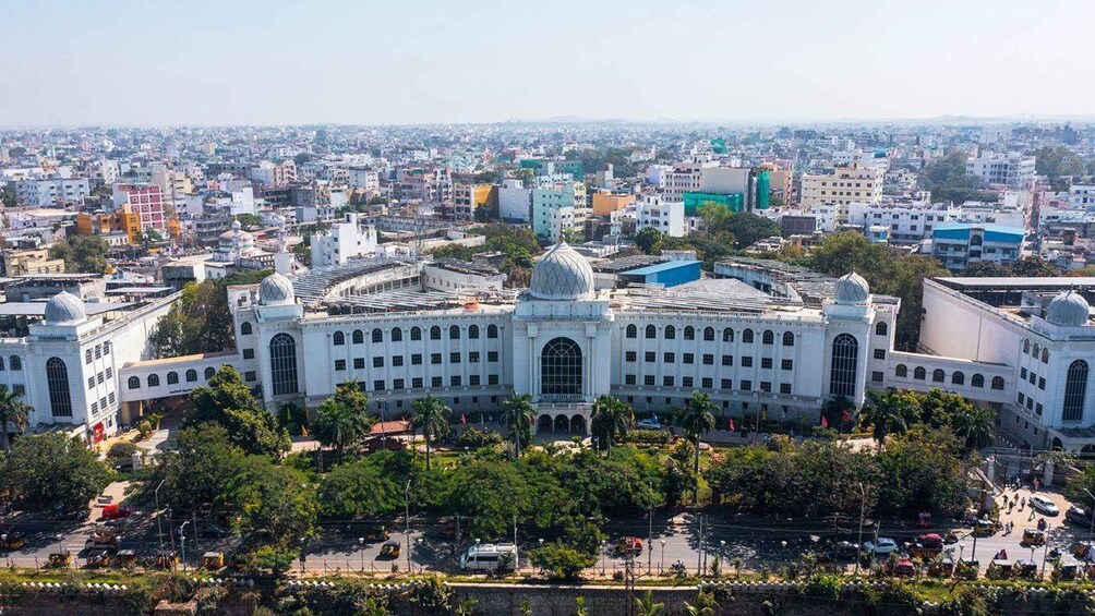 A large white building with a dome and arched windows, surrounded by a busy urban area with many other buildings and vehicles. 5