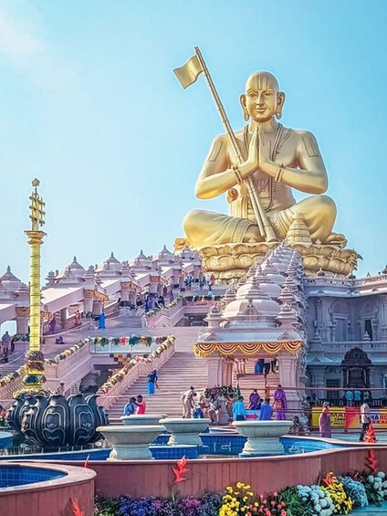 A large golden statue of a seated figure with a flag, surrounded by a temple complex with steps and a pool. 3