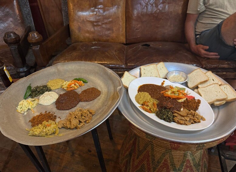 A table with plates of Ethiopian cuisine, including injera, stews, and sides, and a plate of bread and dips. 4
