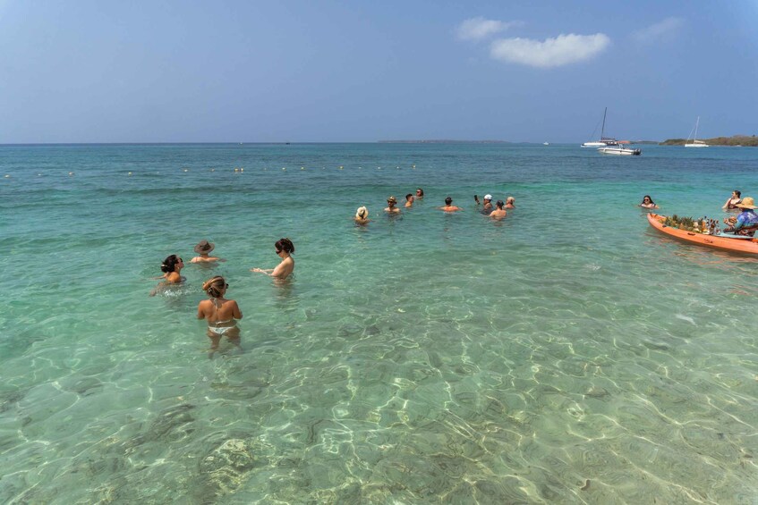 People swimming in clear turquoise water, a boat with passengers, and several anchored boats in the distance. 2