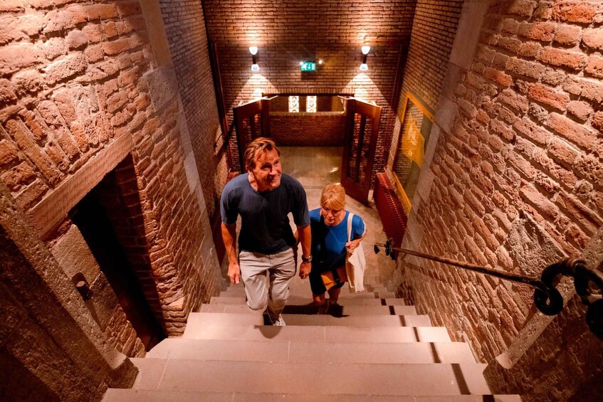 A man and a woman descending a stone staircase with wooden railings and a brick wall. 3