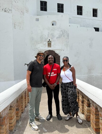 Three people standing in front of a white building with a brick base and a stone archway. 2