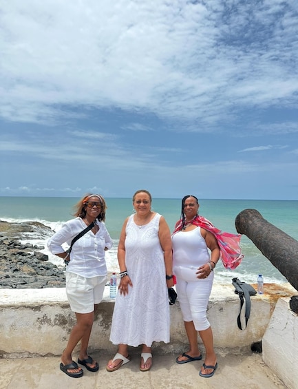 Three people standing on a rocky beach with the ocean in the background. 1
