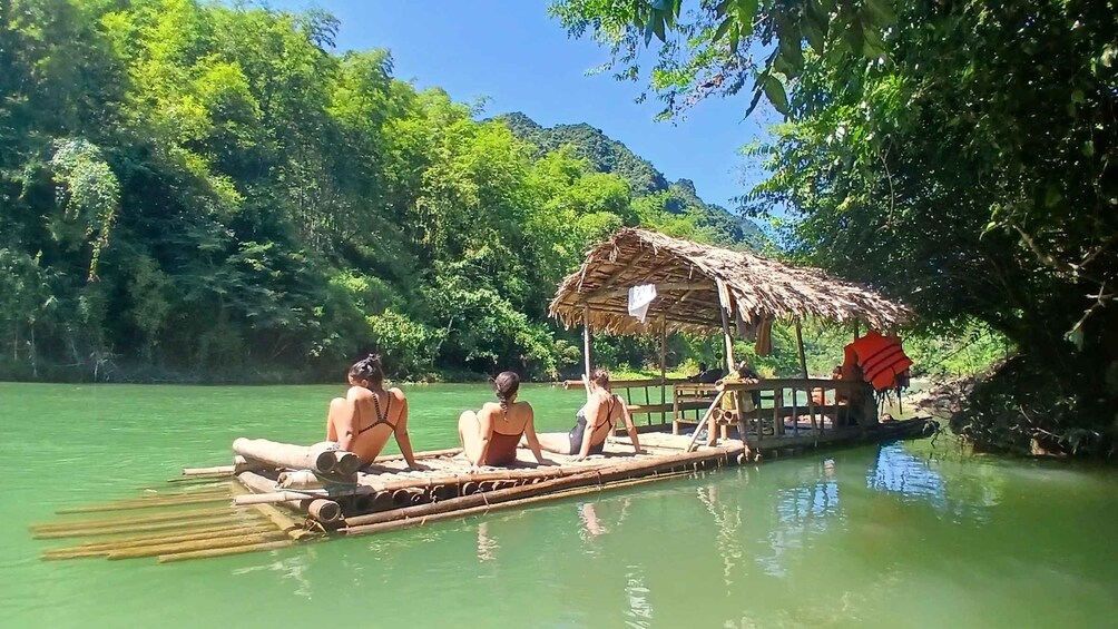 A bamboo raft with a thatched roof on a calm river surrounded by dense greenery. 1