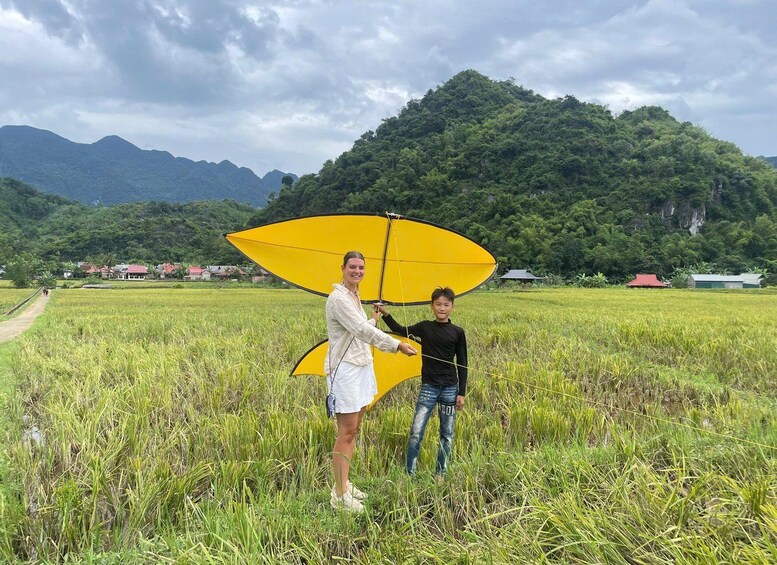 A person holding a yellow kite in a field with mountains in the background. 5