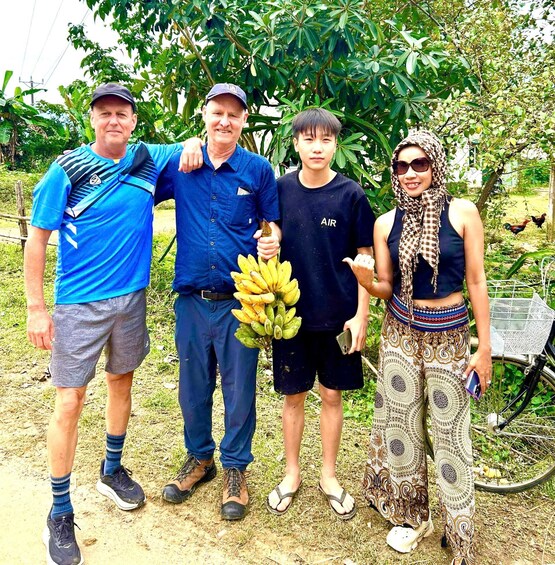 Four people standing outdoors with a bicycle and a tree in the background. 2