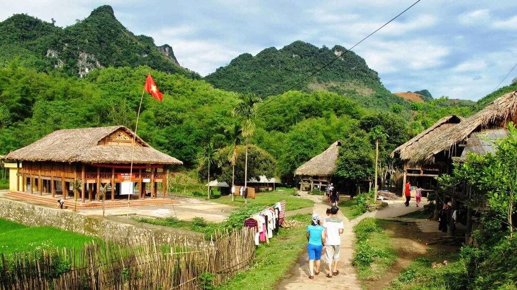 A rural village with thatched-roof houses, a flag, and lush green hills in the background. 1