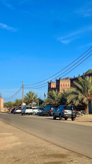A street with parked cars, palm trees, and a large building with a distinctive architectural style. 5
