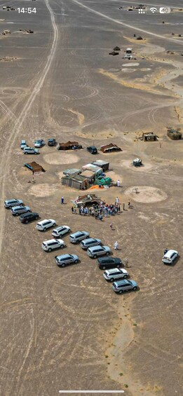 An aerial view of a desert area with a group of people gathered around a central structure, surrounded by parked cars. 3