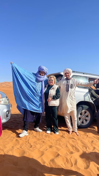 Three people standing in a desert with a white vehicle in the background. 4
