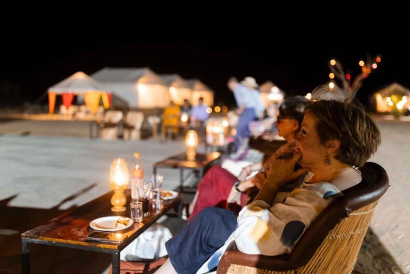 A couple sitting at a table with a candle, overlooking a beach with tents and people in the background. 2
