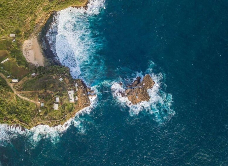 An aerial view of a coastal area with rocky outcrops, a narrow strip of land, and several buildings. 4
