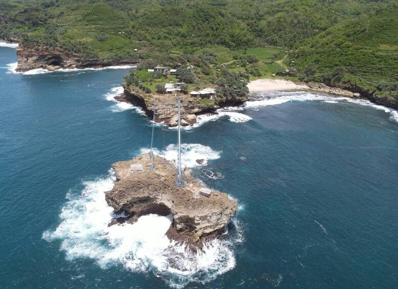 A coastal landscape with a rocky outcrop surrounded by ocean waves, a small settlement with houses, and lush greenery in the background. 3