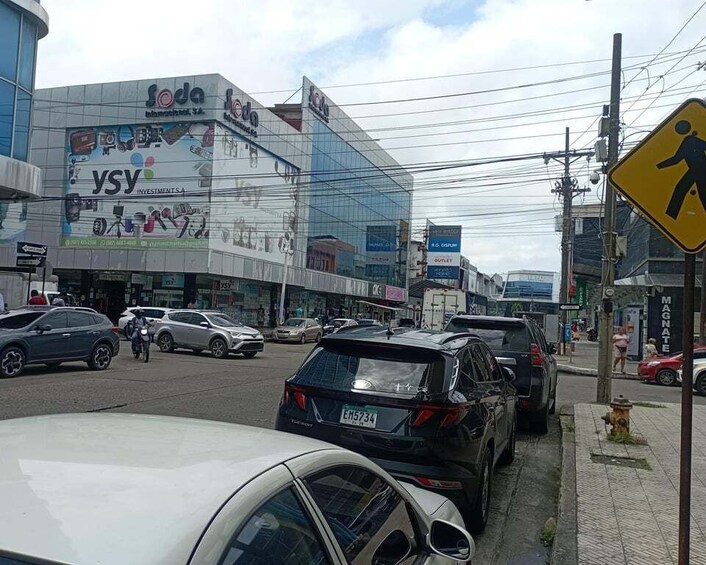 A busy urban street with cars, a pedestrian crossing sign, and commercial buildings with advertisements. 3